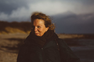 Mature woman wearing warm clothing looking away while standing against cloudy sky