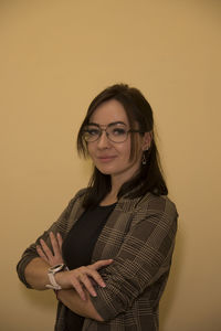 Portrait of smiling young woman with arms crossed standing against yellow background