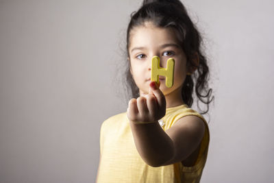 Cute little girl with h letter at hand wearing a yellow dress, indoor isolated portrait