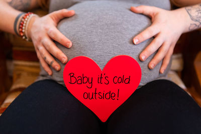 Midsection of pregnant woman with text on heart shape