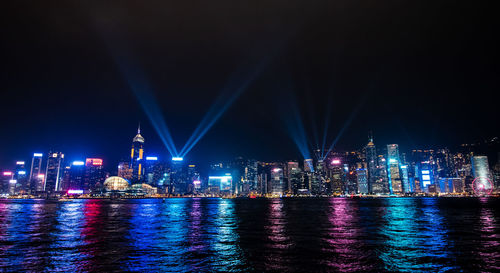 Illuminated buildings by river against sky at night