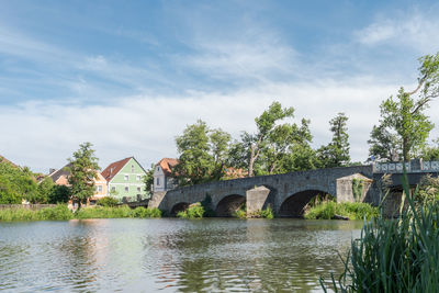 Arch bridge over river by building against sky