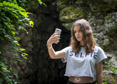 Full length of young woman using phone while standing on tree