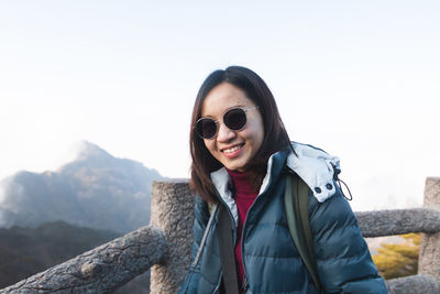 Smiling young woman wearing sunglasses against clear sky