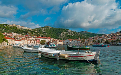 Small boats moored in harbor by city against sky