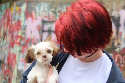 Woman with redhead holding dog against graffiti wall