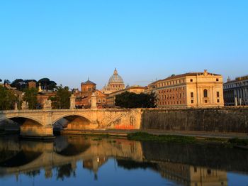 Bridge over river by st peter basilica against clear blue sky in city