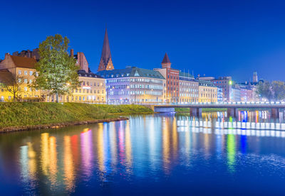 Buildings by river against clear blue sky