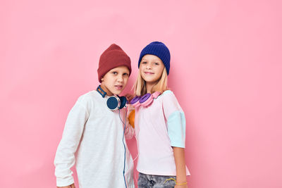 Portrait of sibling wearing headphones against colored background