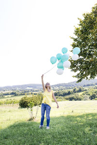 Full length of woman holding balloons against clear sky