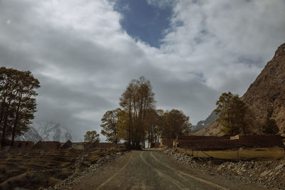 Dirt road amidst trees against sky