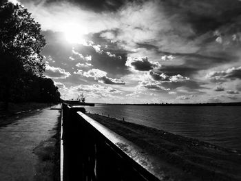 Empty road along calm sea against cloudy sky