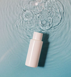 White cosmetic bottle in a blue pool with water and waves. spa skin care.