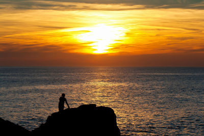 Silhouette man fishing by sea against sky during sunset