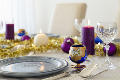 A decorated dining table with candles, cutlery, glasses, colorful christmas balls and gold tinsel