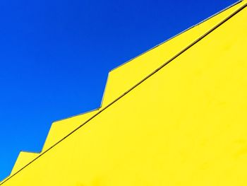 Low angle view of yellow building against clear blue sky