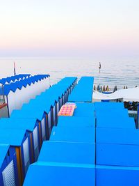 Deck chairs by swimming pool against sea during sunset