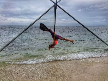 Full length of woman hanging over beach against cloudy sky