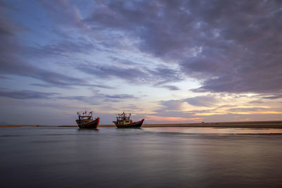 Boats moored in sea against cloudy sky during sunset
