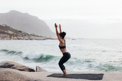 Rear view of woman doing yoga at beach against sky