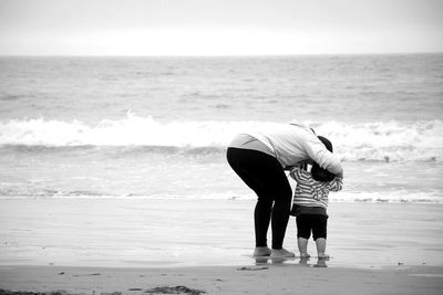 Rear view of woman with baby standing on shore at beach
