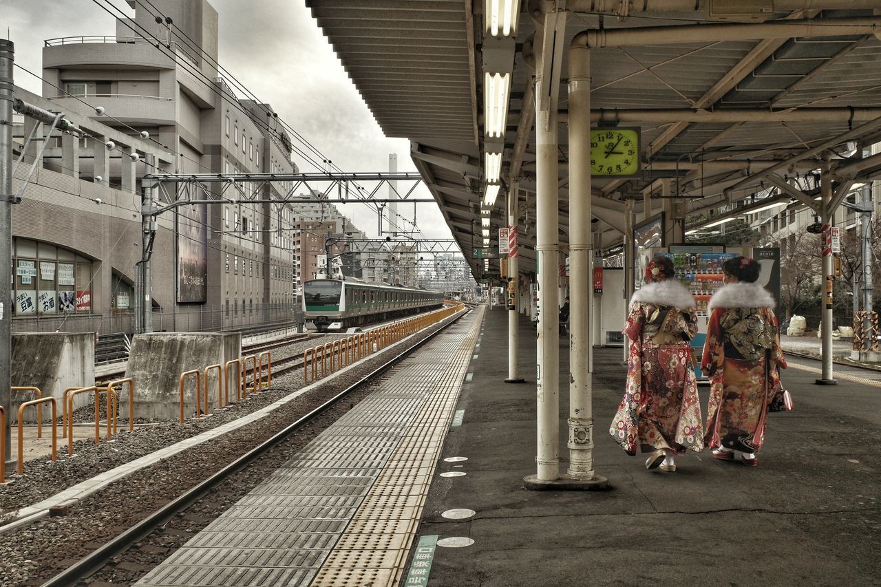 rail transportation, transport, railroad track, track, transportation, architecture, urban area, train station, mode of transportation, adult, public transportation, railroad station, railroad station platform, vehicle, men, women, public transport, group of people, built structure, travel, full length, city, lifestyles, train, day, clothing, rear view, person, railway, outdoors