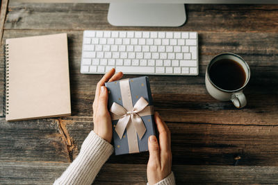 Top view of a gift box in female hands over a working office table.