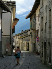 Rear view of woman walking on street amidst buildings in city