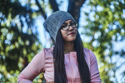 Portrait of young woman standing against tree at park