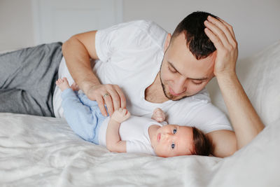 Fathers day. happy proud caucasian father with newborn baby. young man dad parent lying on bed