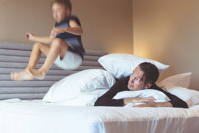 Father lying while son playing on bed at home