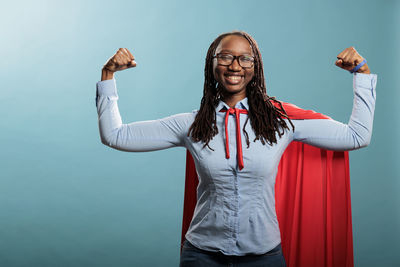 Portrait of smiling young woman with arms raised standing against wall