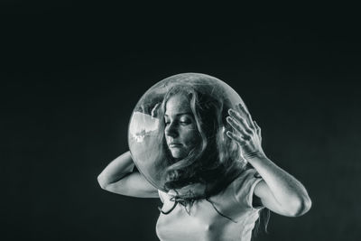 Young woman wearing glass container against black background
