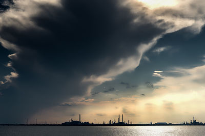 Silhouette buildings by sea against sky during sunset