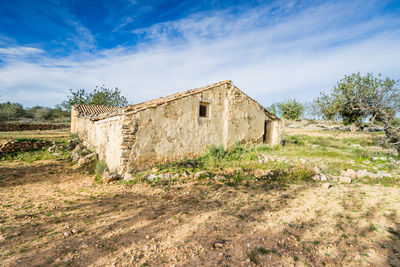 Old house on field by building against sky