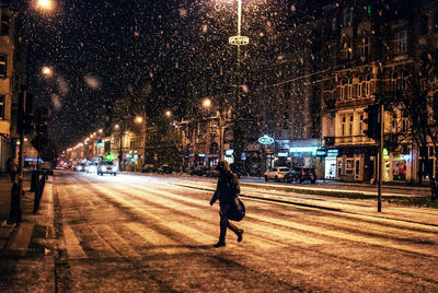 Man zebra crossing on street during snowfall at night