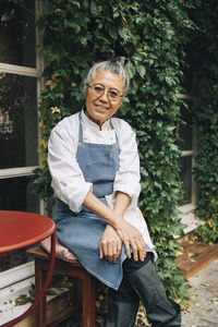 Portrait of smiling senior female chef sitting outside restaurant