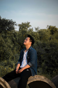 Smiling young man sitting on concrete pipe