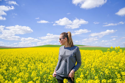 Rear view of young woman standing by yellow flowers on field