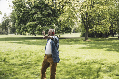 Happy senior man wearing wireless headphones enjoying music at park