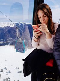 Young woman using mobile phone while sitting in overhead cable car