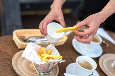 Midsection of man holding french fries with sauce in container over restaurant table