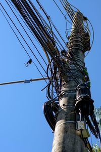 Low angle view of bird perching on cable against clear sky