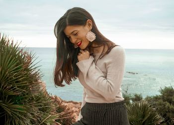 Happy young woman standing by sea against sky