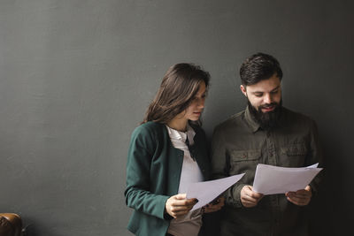 Colleagues doing paperwork while standing against gray background