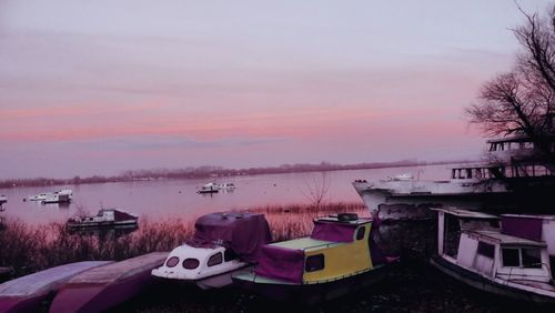 Boats moored on lake against sky at sunset