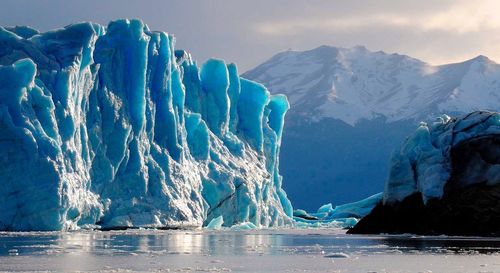 Scenic view of glacier in sea against snowcapped mountains