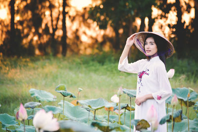 Beautiful woman wearing conical hat standing amidst lotus buds