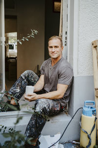 Portrait of smiling male carpenter holding coffee cup at doorway of house