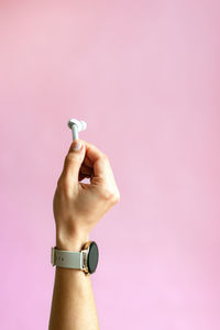 Close-up of hand holding cigarette against pink background